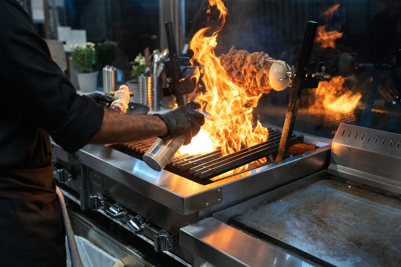 Un cuisinier saisit de la viande sur un grill, flammes en cuisine (photo d’illustration)