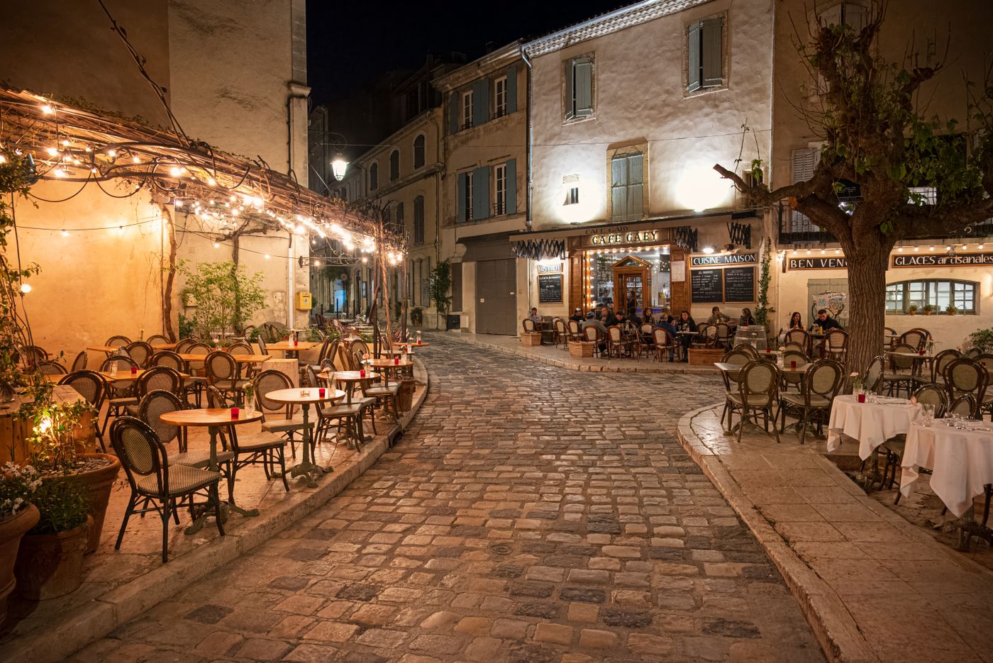 Rue pavée de Provence éclairée le soir, terrasses de café (photo d’illustration)